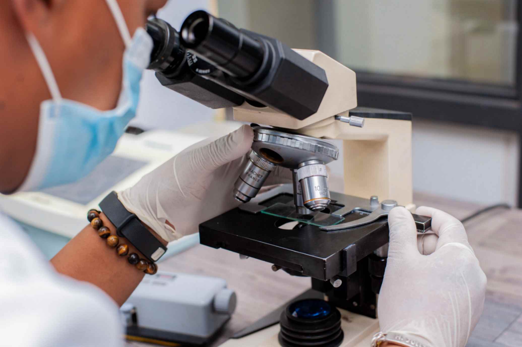Une assistante de laboratoire ajuste le microscope avec un échantillon sur une lame en gros plan de laboratoire.